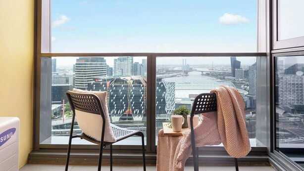 Ein Balkon mit zwei Stühlen, einem kleinen Tisch mit einer Pflanze und Blick auf eine Stadtlandschaft mit Gebäuden und einem Fluss.