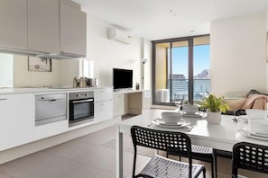 A modern kitchen with white cabinetry, a built-in oven, and a flat-screen TV. - Southern Cross Gem: Modern Home with Harbour Views (Melbourne)