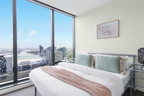 A modern hotel room with a large bed, a view of the city, and a framed picture on the wall.