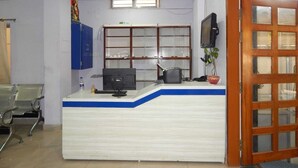 Um balcão de recepção com um computador, um armário azul, uma janela e uma televisão.