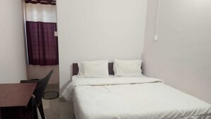 Quarto pequeno e limpo com uma cama, uma escrivaninha e uma cadeira.