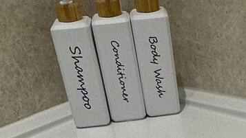 Drie toiletartikelen – shampoo, conditioner en douchegel – op een witte ondergrond voor een betegelde muur.