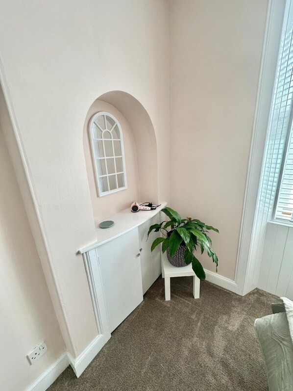 A corner room with a white arched window, a small white table with a plant, and a grey carpet. - The Prestwick Retreat (Prestwick)