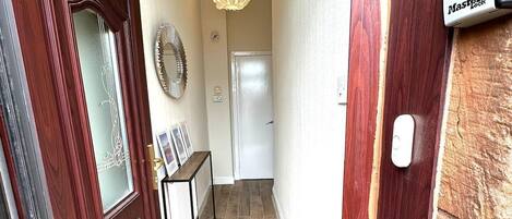 Un pasillo con puerta de madera, felpudo, timbre y buzón.