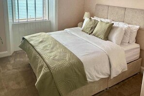 A bedroom with a bed, a window with blinds, and a carpeted floor. - The Prestwick Retreat (Prestwick)