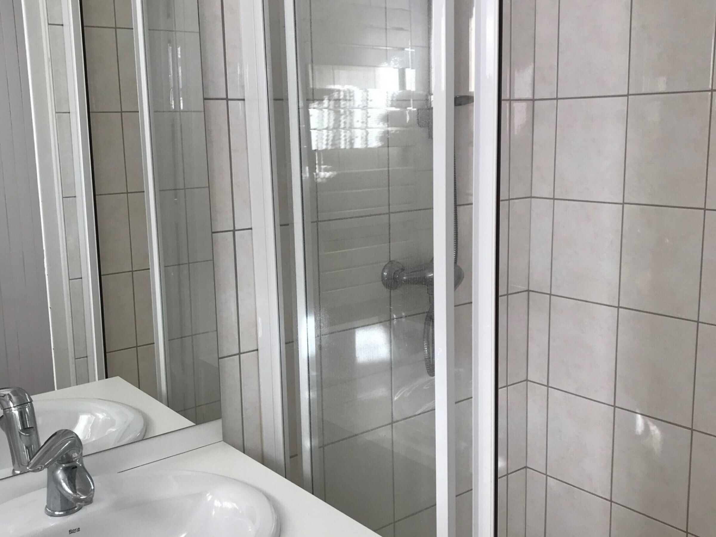 Een badkamer met een wit wastafelmeubel, een spiegel en een douchecabine van glas.