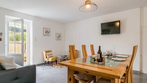 Zona pranzo moderna con tavolo in vetro, sedie in legno e televisore a parete.