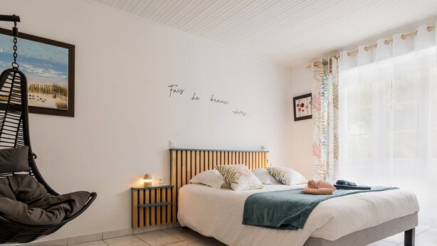 Camera da letto con un letto, una poltrona sospesa, un comodino e una parete con un testo parziale.
