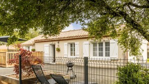 Una casa con tetto in tegole, un patio recintato con sedie e un'area giardino.