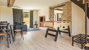 Un salon moderne avec un baby-foot, un coin repas comprenant des chaises et une table, et un escalier au design original.