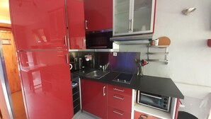 A compact kitchen with red cabinets, a stainless steel sink, and a microwave.