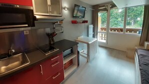 A compact kitchen with a microwave, stove, and red cabinets. A small table and a TV are mounted on the wall.