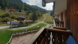 A balcony with a view of a mountain landscape, a ski lift, and a small building with a sign.