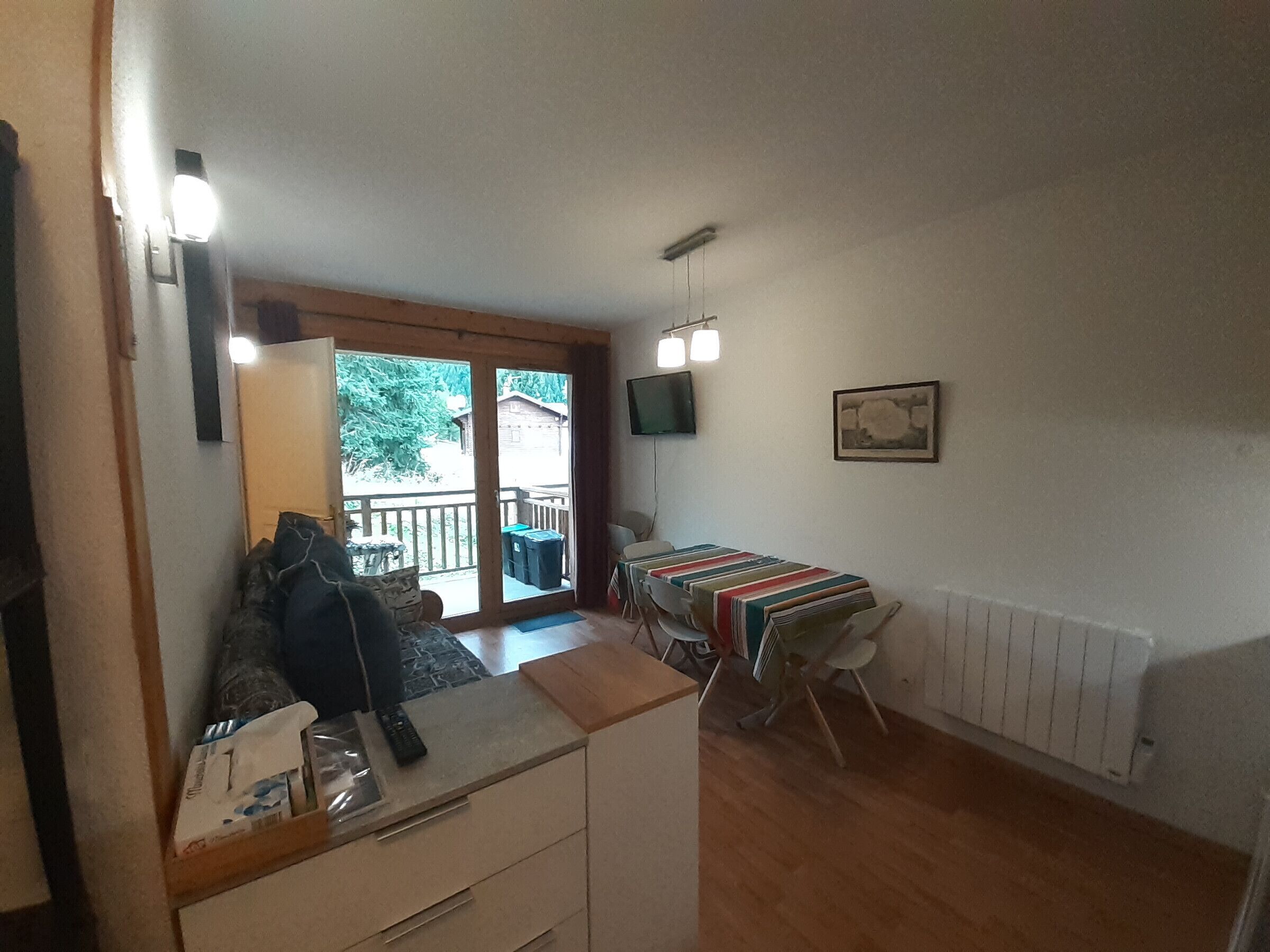 A compact living space with a kitchenette, a dining area with a table and chairs, a TV mounted on the wall, and a sliding glass door leading to an outdoor area.