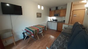 Un espace de vie compact comprenant un coin cuisine, un coin repas avec une table et des chaises, un canapé et un téléviseur fixé au mur.