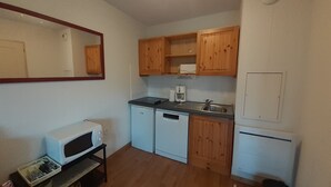 Una cocina compacta con armarios de madera, un microondas, un lavavajillas y un refrigerador.