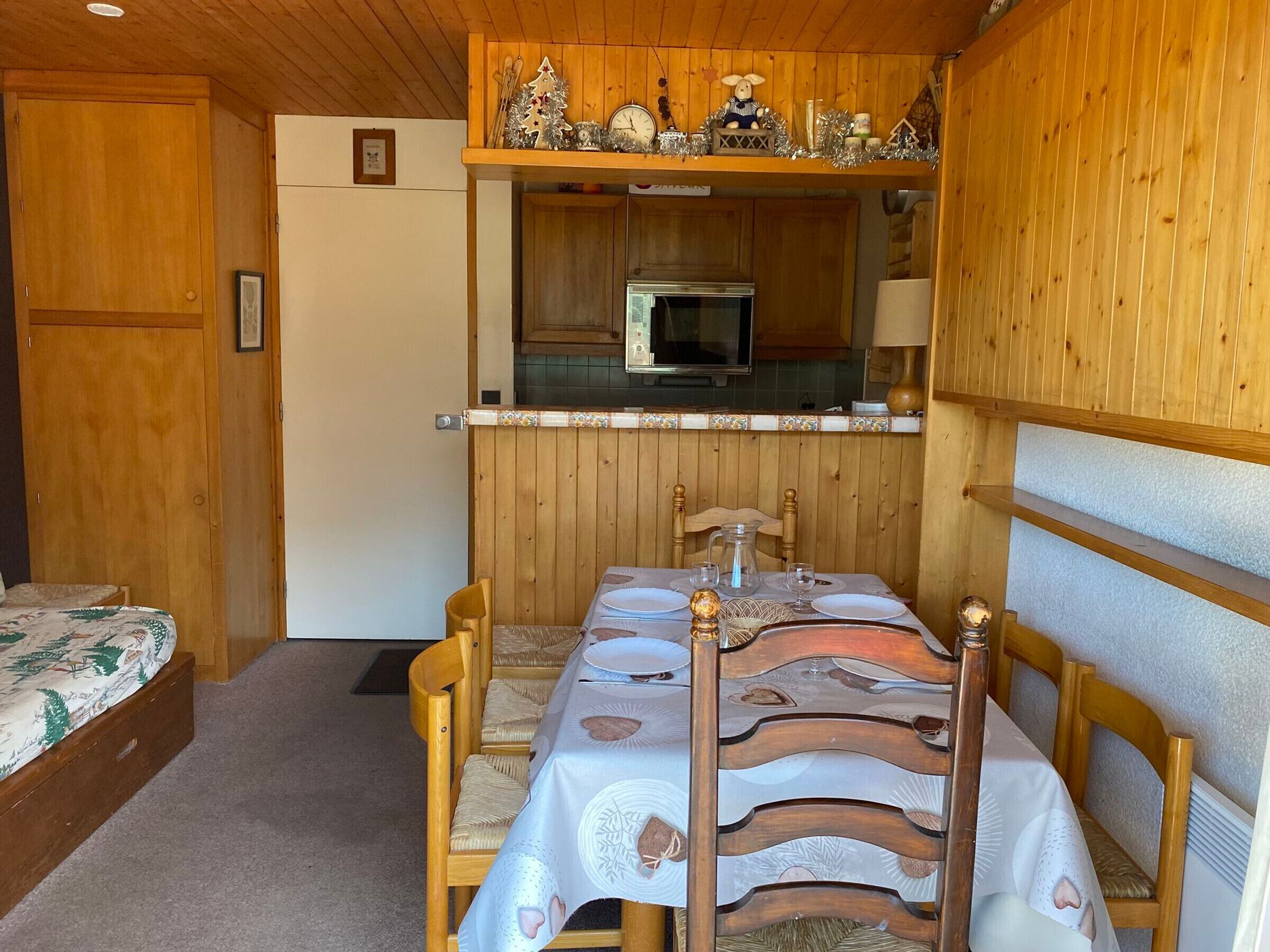 A cozy cabin-style room with a wooden interior, a dining table set for four, and a kitchenette with a microwave and a small refrigerator.