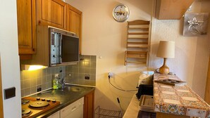 A compact kitchen with wooden cabinets, a microwave, a sink, and a clock on the wall.