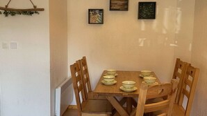 Zona de menjador amb taula de fusta preparada per a quatre persones, rodejada de cadires de fusta. Hi ha obres d'art emmarcades a la paret sobre la taula.