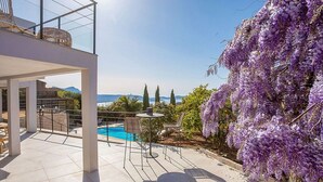 A modern outdoor patio with a pool, seating, and a view of the sea and mountains. - Superb 6 Bedroom Villa, Sea View, Swimming Pool & Pétanque, 5mn from the Beach (Lumio)
