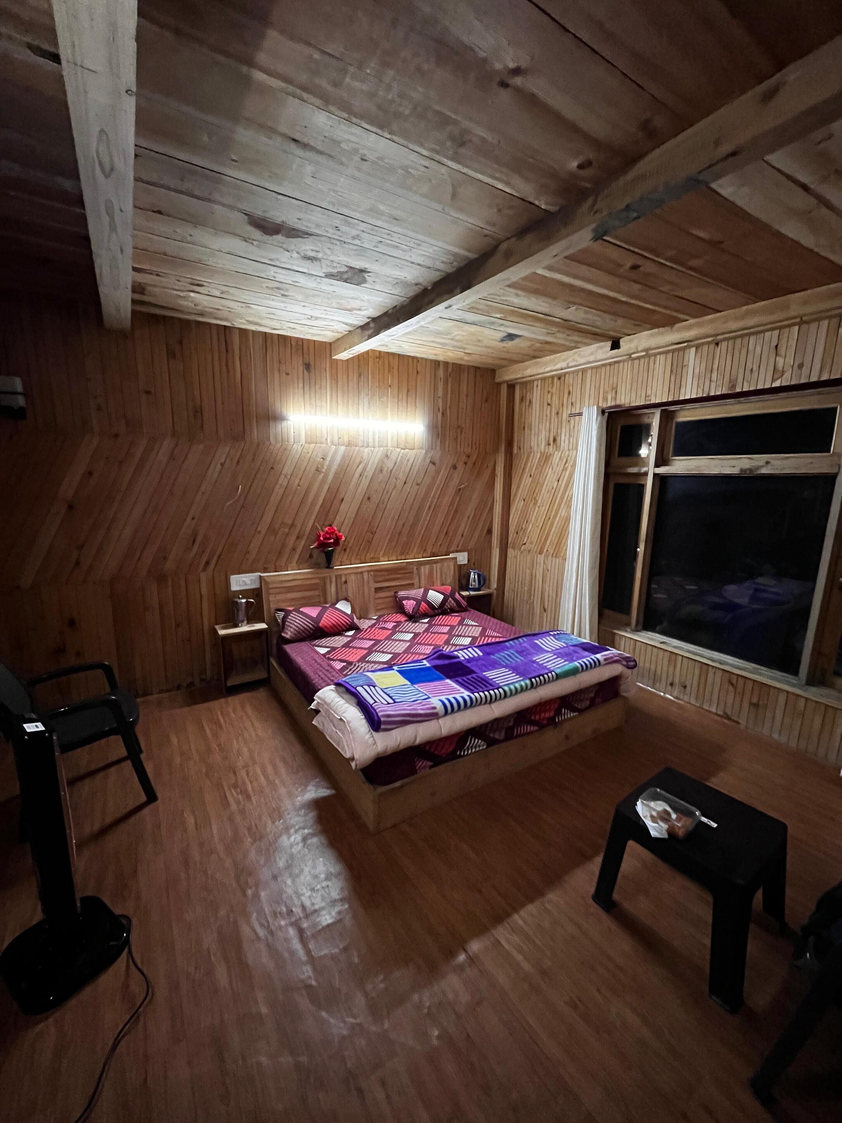 Une pièce aux murs lambrissés, contenant un lit, une petite table, une chaise et une fenêtre.