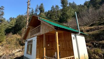 A wooden cabin with a green roof, surrounded by trees and a stone pathway.