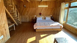 Ein Schlafzimmer einer Holzhütte mit einem Bett, einem Nachttisch, einer Lampe und einem Fenster.