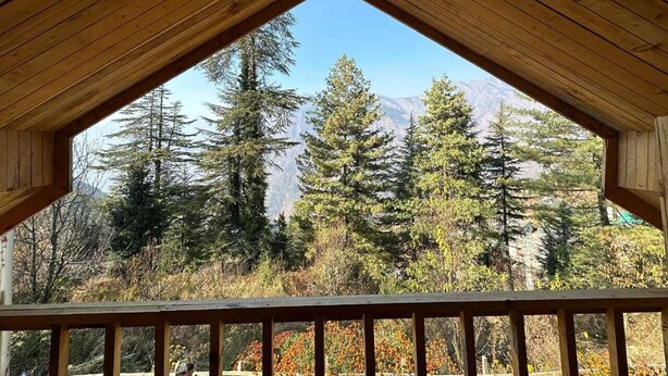 Eine Holzhütte mit Satteldach und einem Balkon mit Blick auf eine bewaldete Landschaft und Berge im Hintergrund.