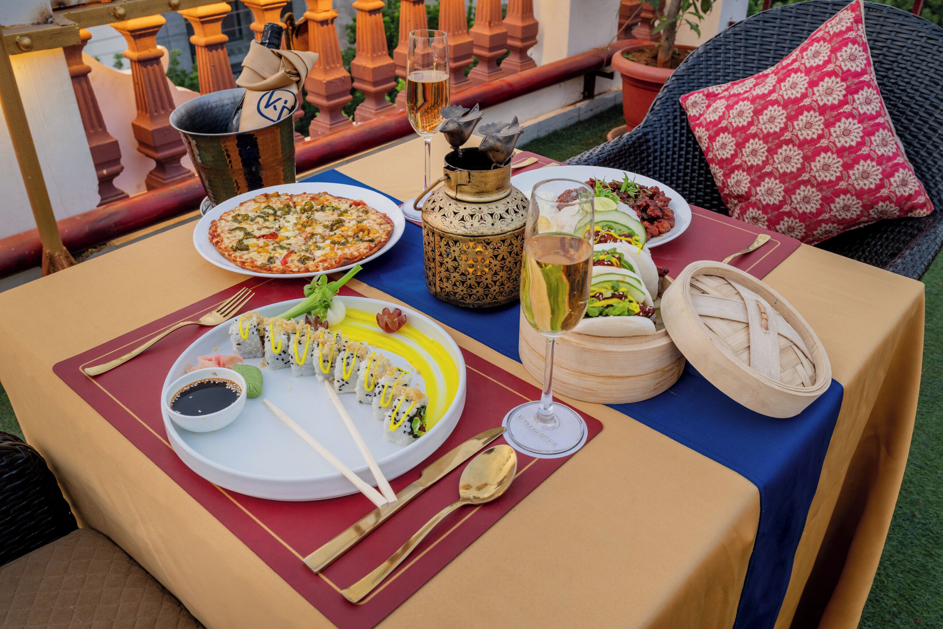 Et bord dækket med et udvalg af retter, herunder sushi, pizza og en salat, samt drikkevarer og en dekorativ lanterne.