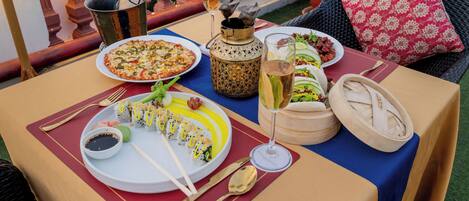 Et bord dækket med et udvalg af retter, herunder sushi, pizza og en salat, samt drikkevarer og en dekorativ lanterne.