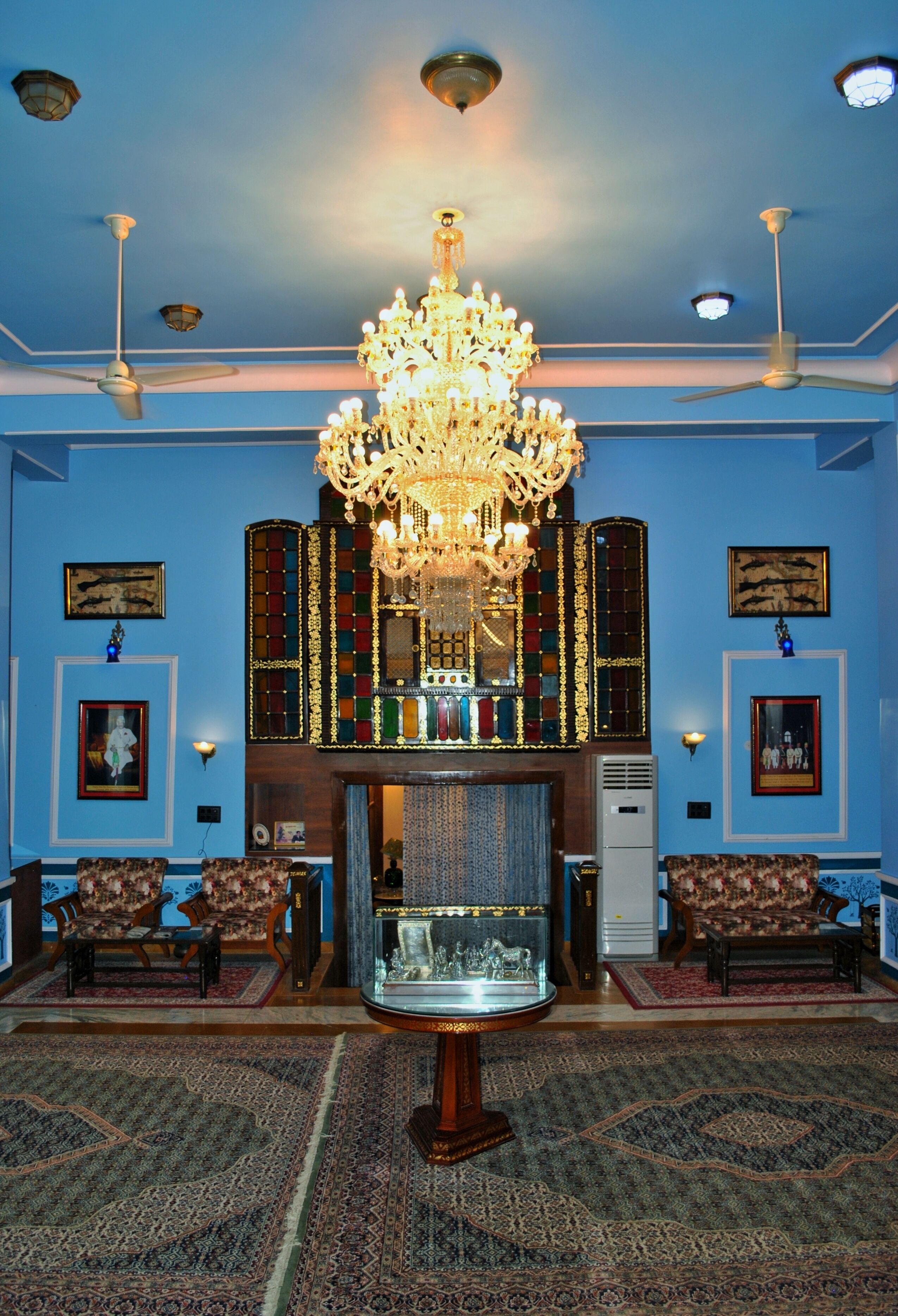 A room with a chandelier, two sofas, a fireplace, and a large rug.
