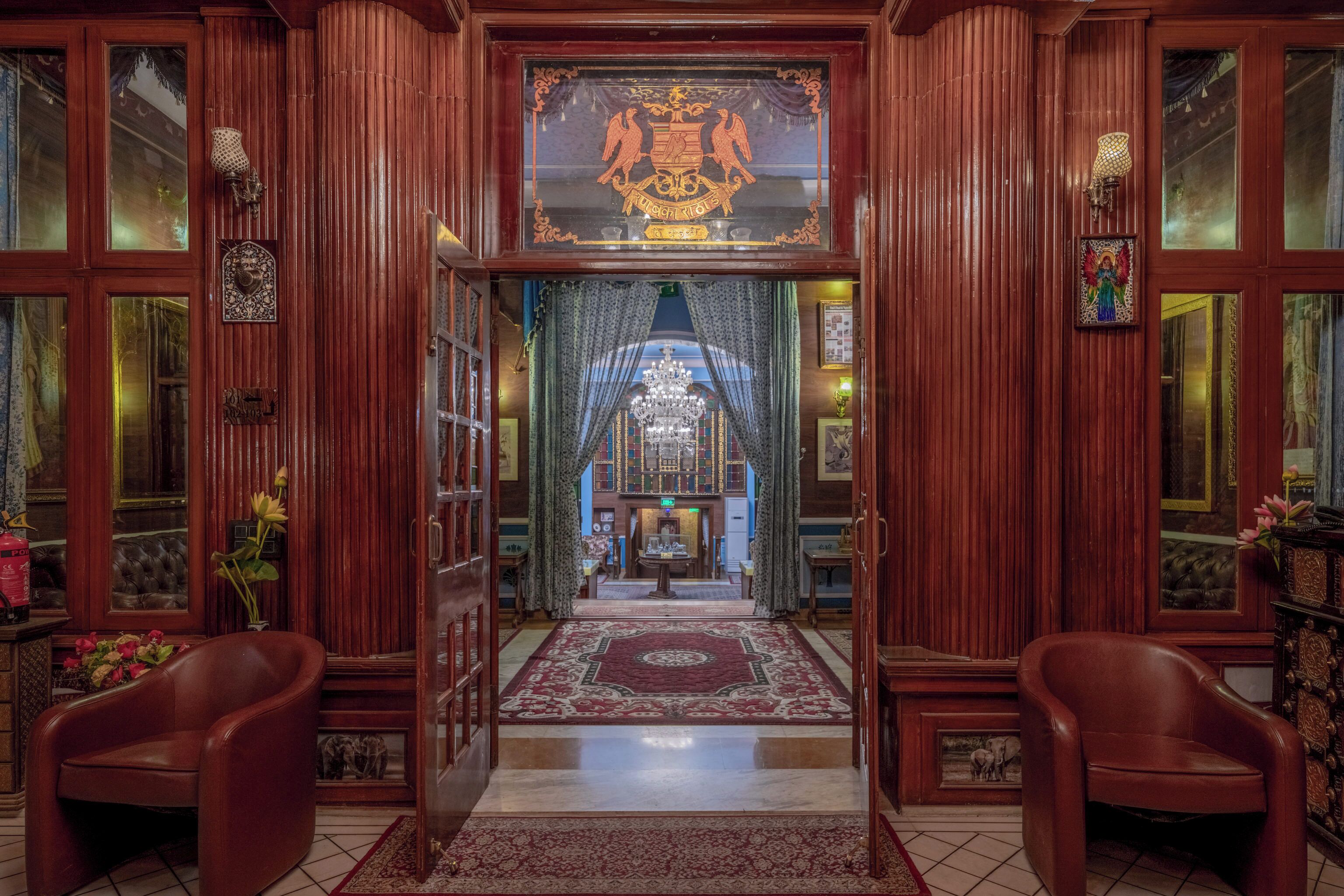 Una entrada imponente con puerta de madera, candelabro y alfombra roja que conduce a un salón con candelabro.