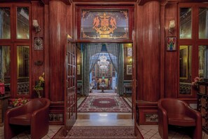 A grand entrance with a wooden door, a chandelier, and a red carpet leading to a room with a chandelier. - WelcomHeritage Kurki Palace (Jaipur)