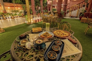 A table set with various dishes and a menu, surrounded by ornate chairs and a decorative backdrop. - WelcomHeritage Kurki Palace (Jaipur)