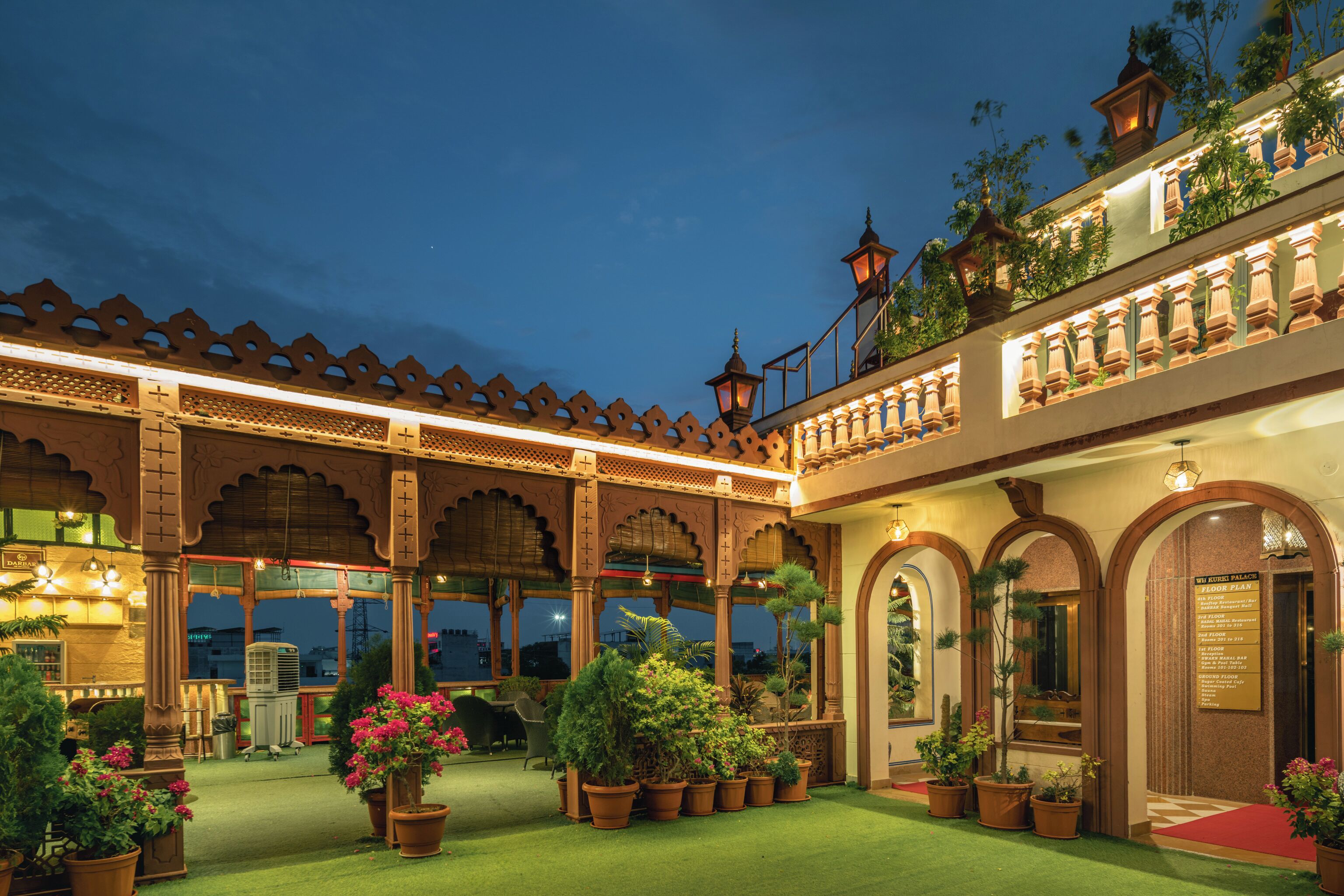Un patio de hotel con zona de estar cubierta, plantas en macetas y un letrero que indica el plano de pisos.