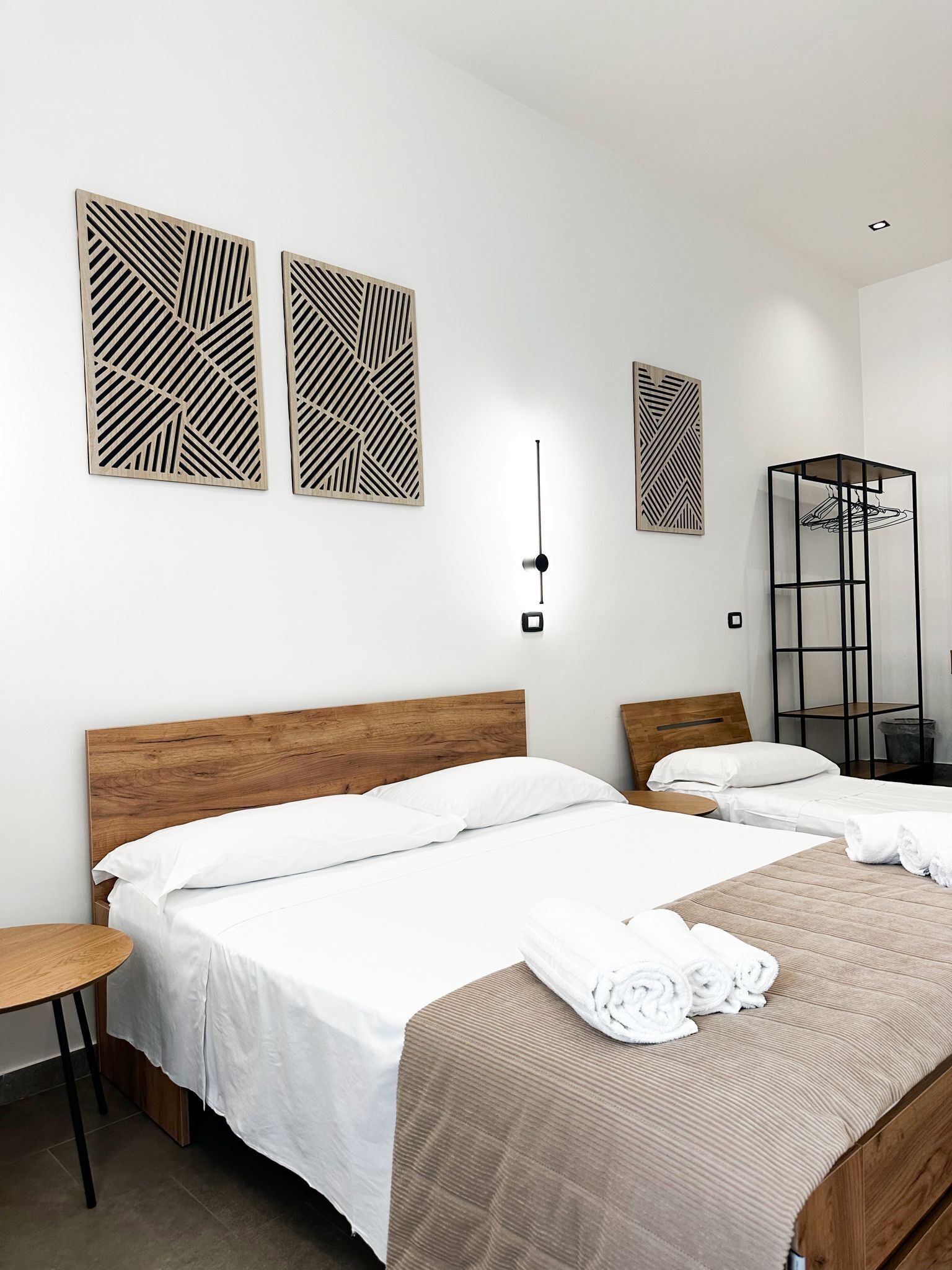 A hotel room with two beds, a wooden headboard, a bedside table, a mirror, and geometric wall art.