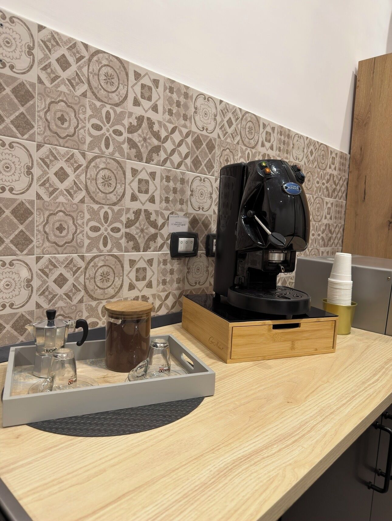 A kitchen counter with a coffee machine, a kettle, a glass carafe, and a coffee grinder.