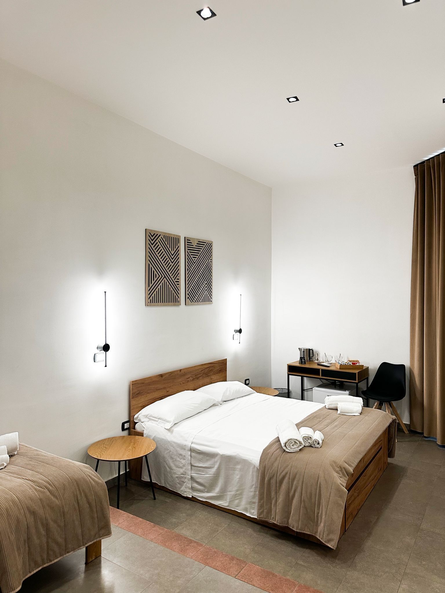 Una camera d'albergo con un letto centrale, due comodini, una scrivania e una sedia.