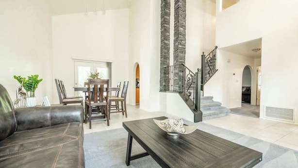 A spacious living room with a dark leather sofa, a wooden coffee table, and a staircase with stone accents. - Large Family Home with Game Room (Page)