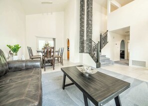 A spacious living room with a dark leather sofa, a wooden coffee table, and a staircase with stone accents. - Large Family Home with Game Room (Page)