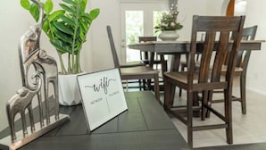 A dining table with a laptop displaying 'wifi' and 'network' text, surrounded by chairs and potted plants. - Large Family Home with Game Room (Page)