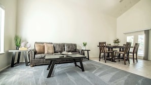 A spacious living room with a leather sofa, a coffee table, and a dining area with wooden chairs and a table. - Large Family Home with Game Room (Page)