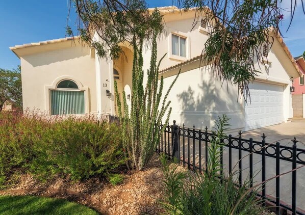 A two-story house with a garage, surrounded by a black wrought iron fence and various plants. - Large Family Home with Game Room (Page)