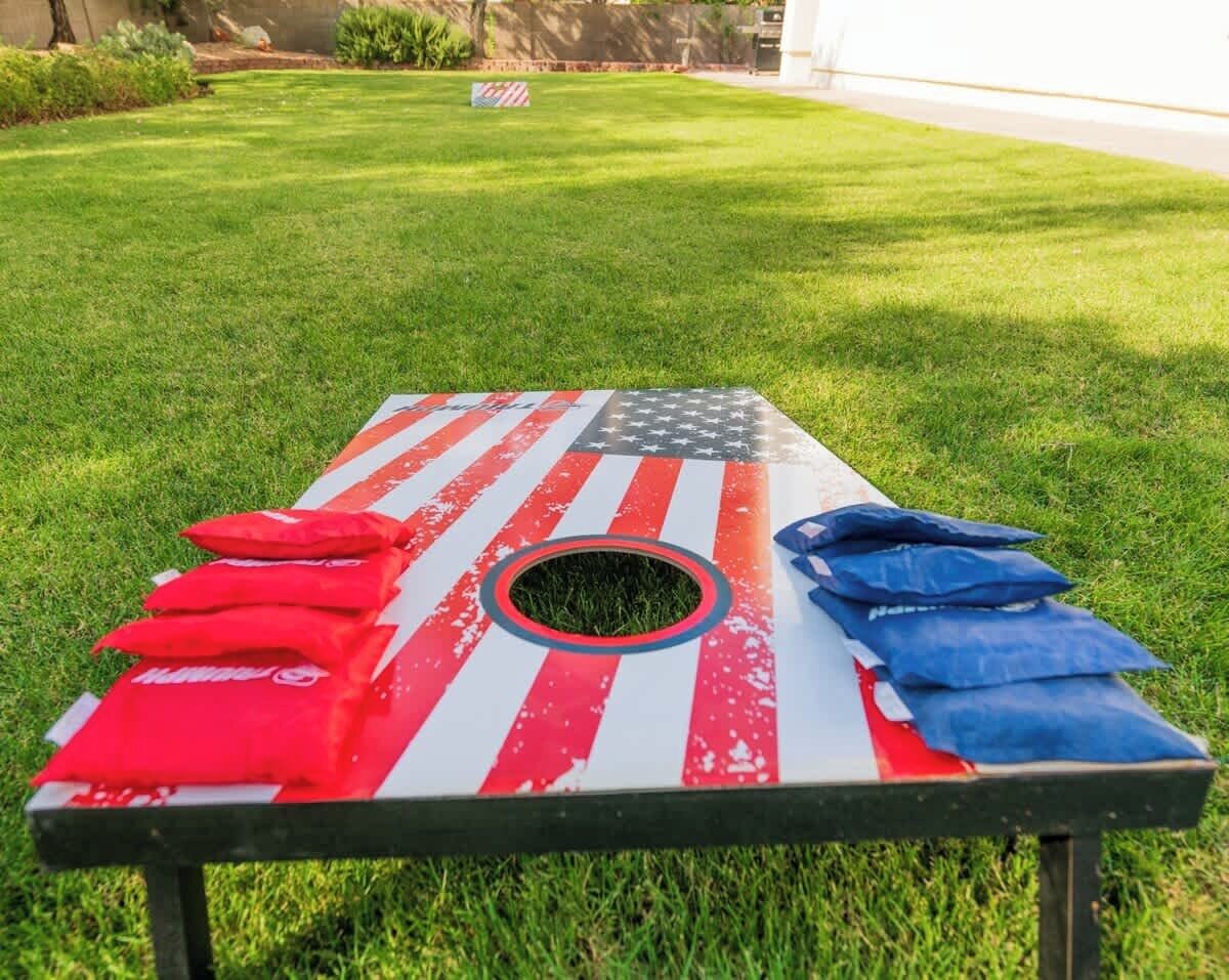 A table with an American flag design, surrounded by red and blue bags, set on a grassy lawn.