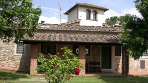 A two-story building with a tiled roof, stone walls, and a small garden area with a tree and a flower pot.