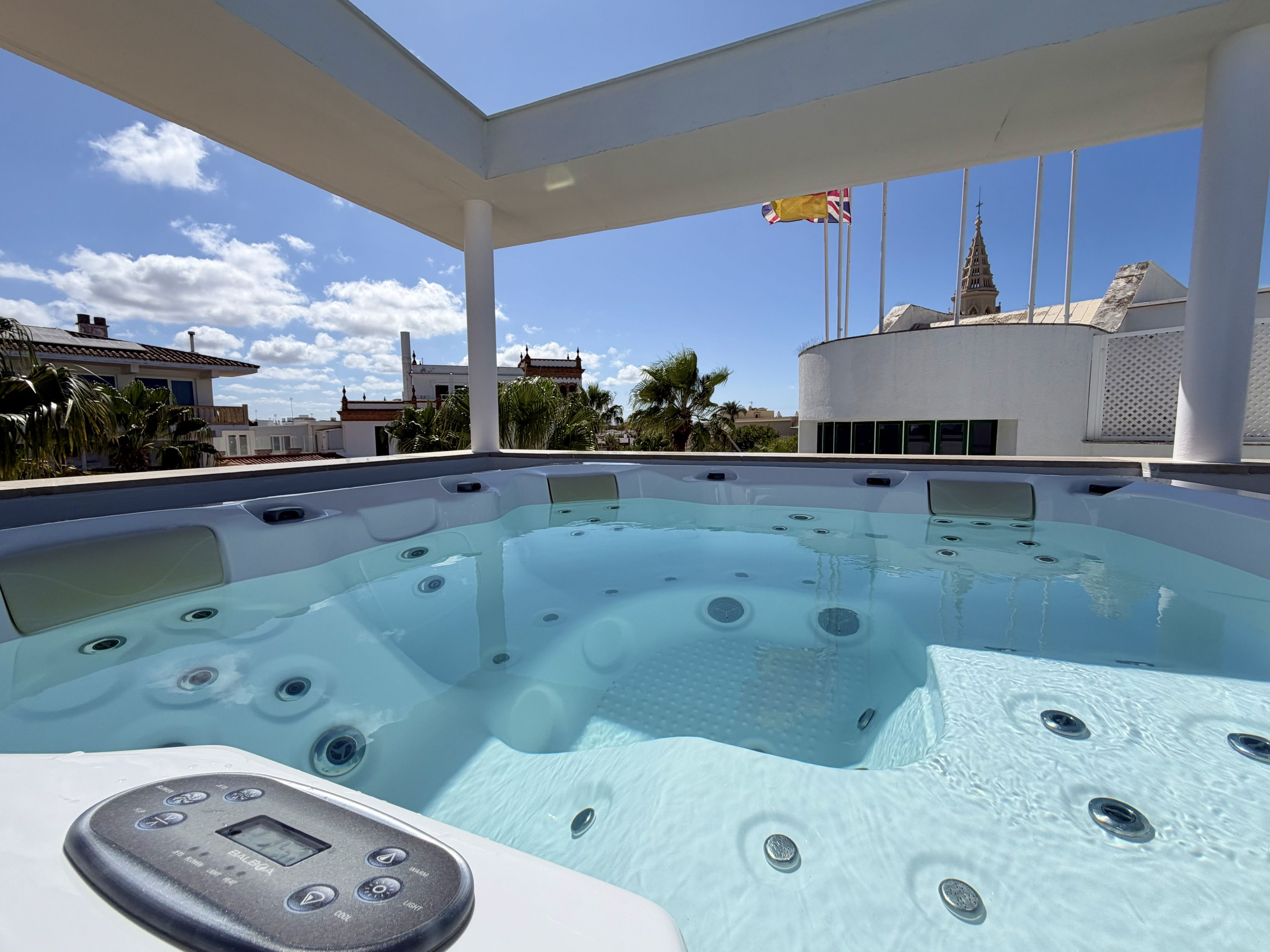 Piscina en la azotea con jacuzzis, un panel de control digital y vistas a edificios y palmeras.