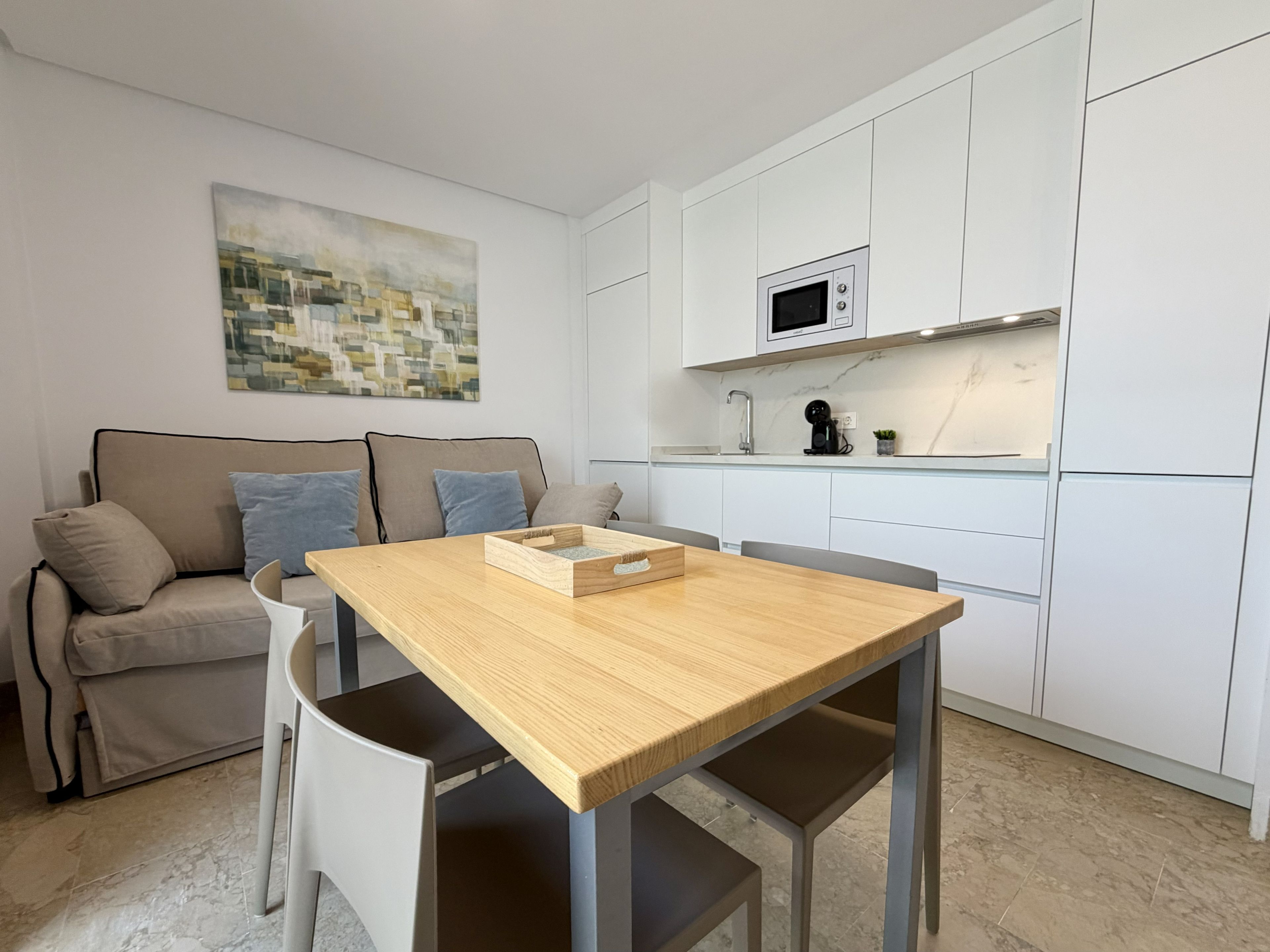 Una cocina moderna con armarios blancos, una mesa de comedor de madera y un sofá gris.