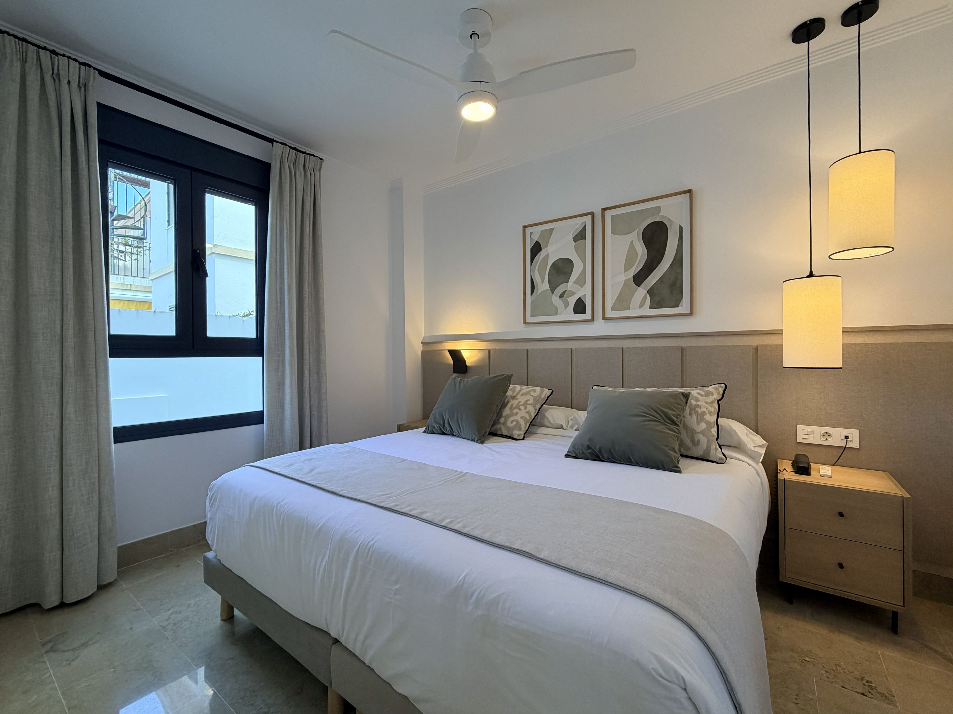 A hotel room with a bed, a nightstand, a ceiling fan, and artwork on the wall.