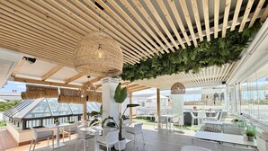 Un espacio exterior para comer con suelo de madera, mobiliario blanco y vistas a la ciudad.
