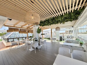 Un espace de restauration en plein air doté d’un plancher en bois, de mobilier blanc et offrant une vue sur le paysage urbain.